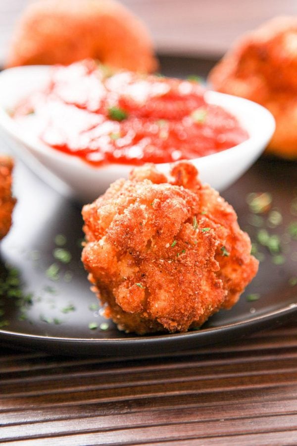 A deep fried macaroni and cheese ball being dipped in marinara.