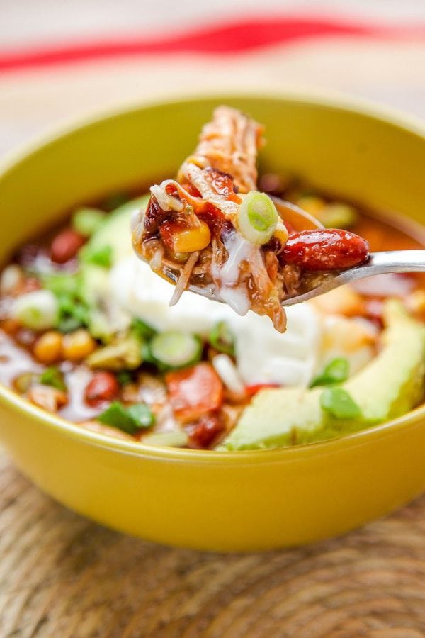 a spoon with a bite taco soup containing chicken, beans, corn, and green onion.