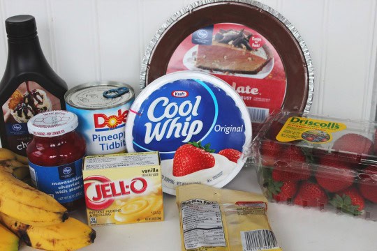 ingredients including Cool Whip, vanilla pudding, bananas, strawberries, cherries, and chocolate syrup.