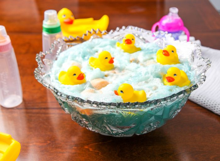 a bowl of blue baby shower punch topped with rubber ducks and surrounded by baby bottles. 