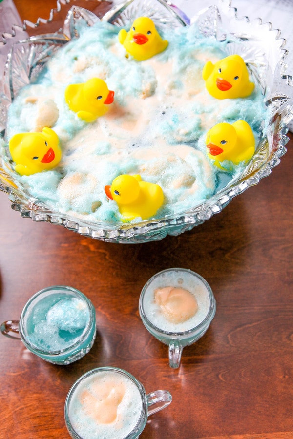 a glass punch bowl with with blue punch, sherbet, and floating rubber ducks. 