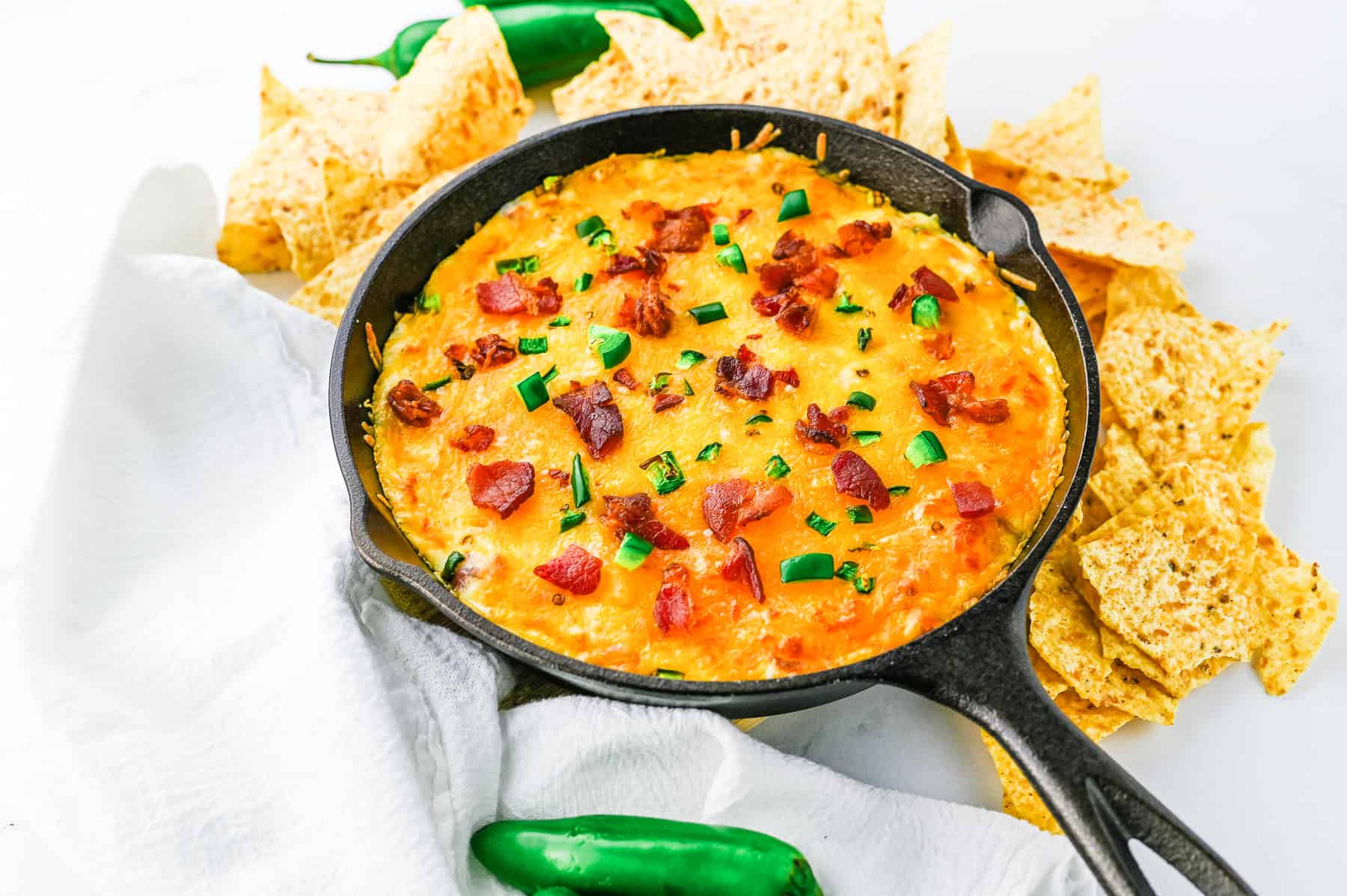 jalapeno popper dip with bacon and green onions in a skillet surrounded by tortilla chips.