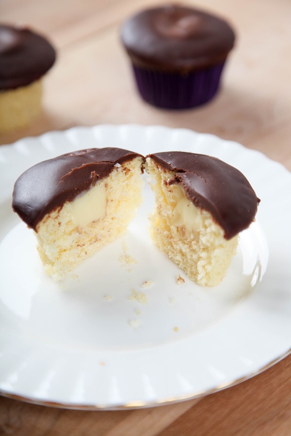a cupcake topped with chocolate ganache cut in half to reveal a pastry cream center.