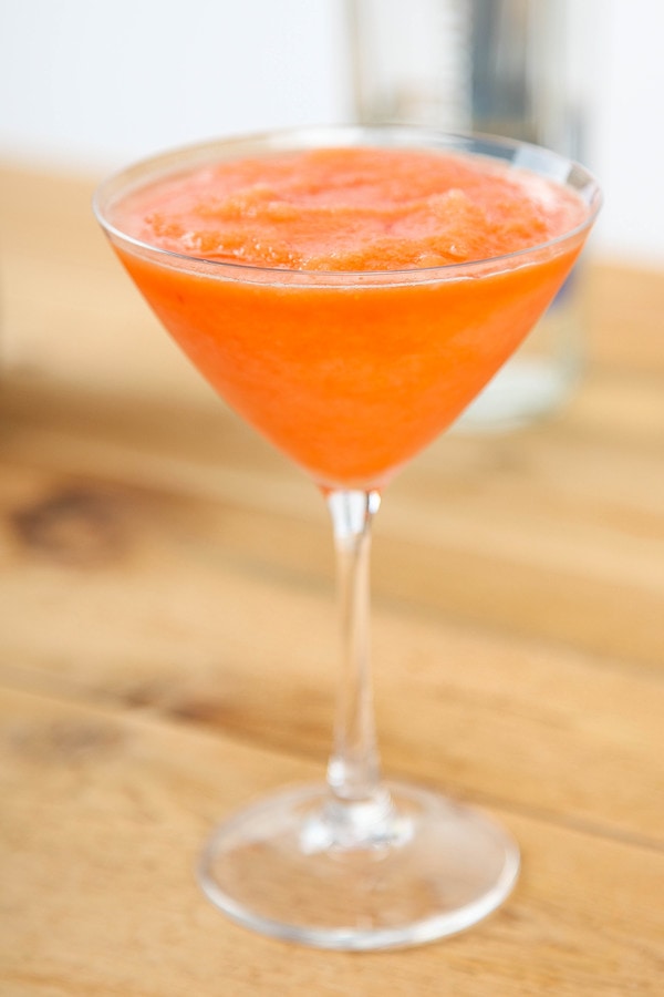 a wine glass containing a frozen peach asti cocktail on a wooden table.