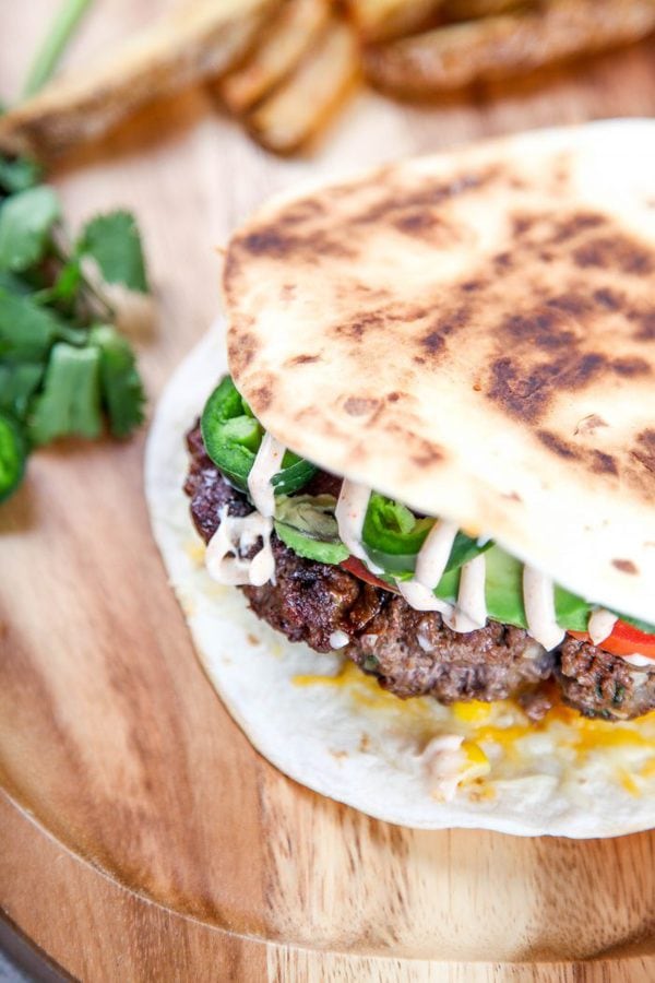 an overhead view of a quesadilla with flour tortillas, burgers, jalapeno, and avocado on a wooden surface. 
