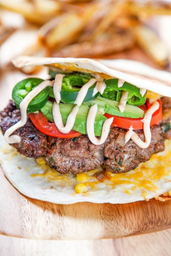 a burger topped with tomato, avocado, and jalapeños between 2 grilled tortillas. 