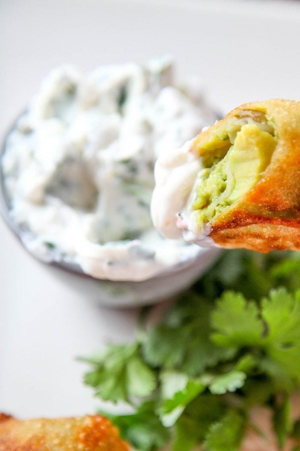 an egg roll filled with avocado being dipped into a creamy cilantro sauce.