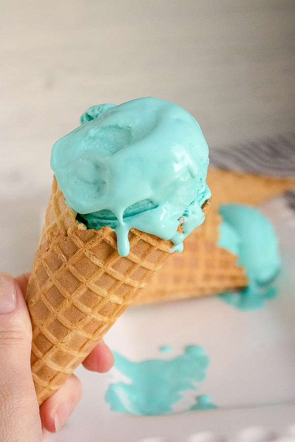 a hand holding a waffle cone filled with blue moon ice cream.