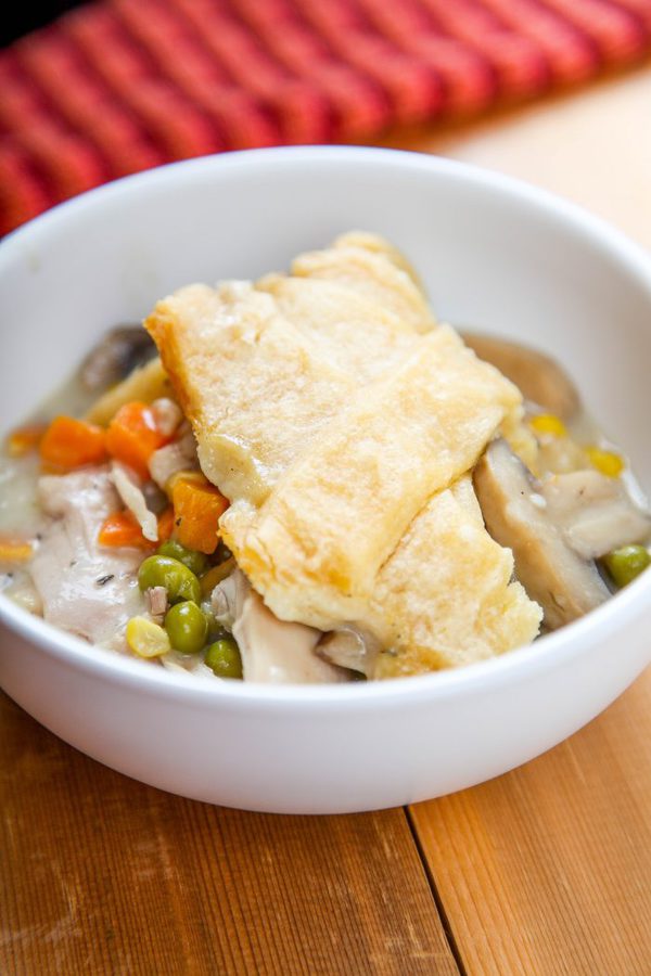 a close up of chicken pot pie with carrots, peas, corn, and a crescent roll topping.