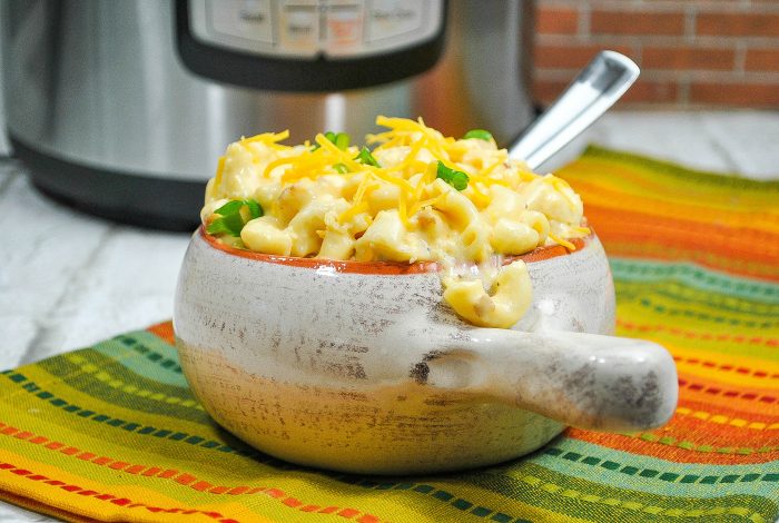 mac and cheese in a white and orange bowl with a handle with a silver spoon stuck inside.