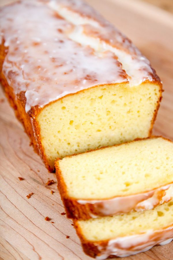 a lemon pound cake topped with a lemon glaze with 2 slices lying in front of the cake. 