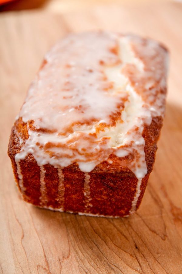 a lemon pound cake drizzled with lemon glaze sitting on a wooden table. 