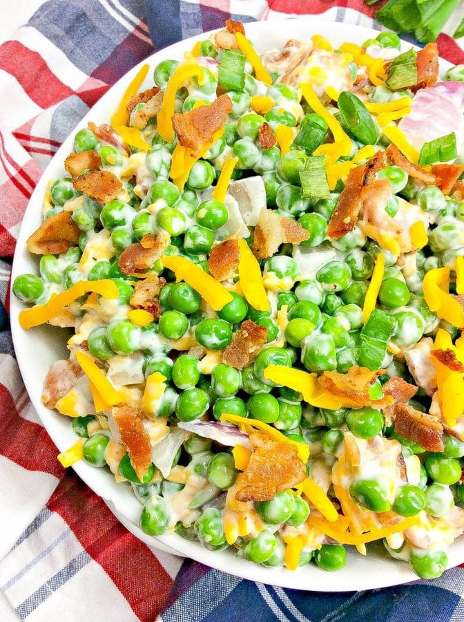 a large bowl of pea salad topped with bacon and shredded cheese on a patriotic napkin.