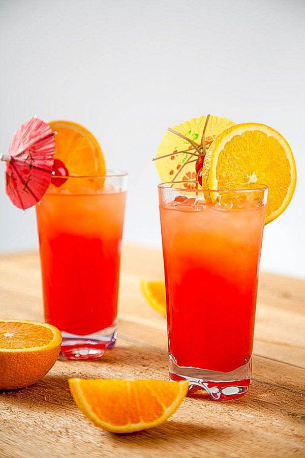 two tequila sunrise drinks topped with cocktail umbrellas and a slice of orange. 