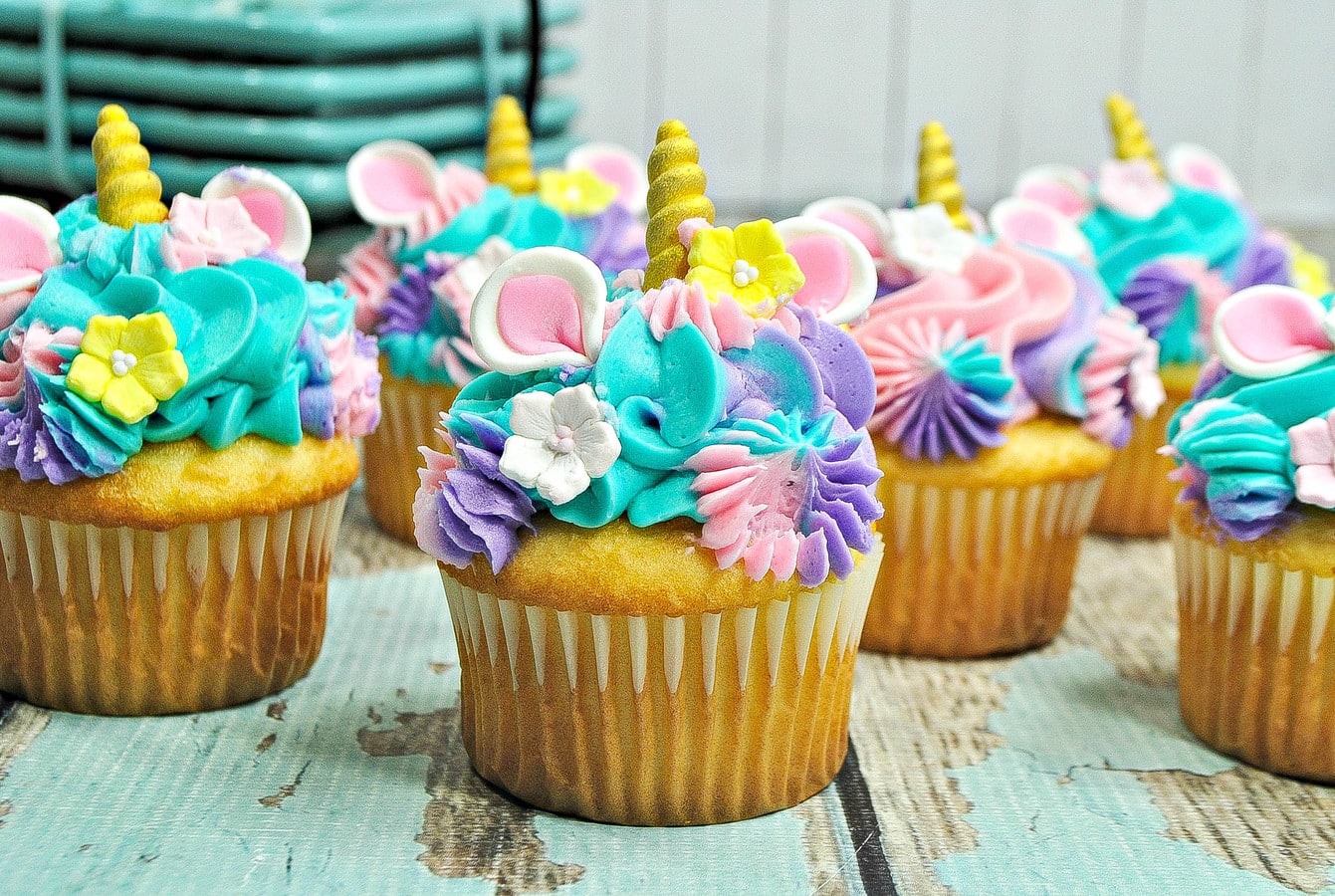yellow cupcakes with multicolored frosting, unicorn horns, unicorn ears, and decorative sugar flowers. 