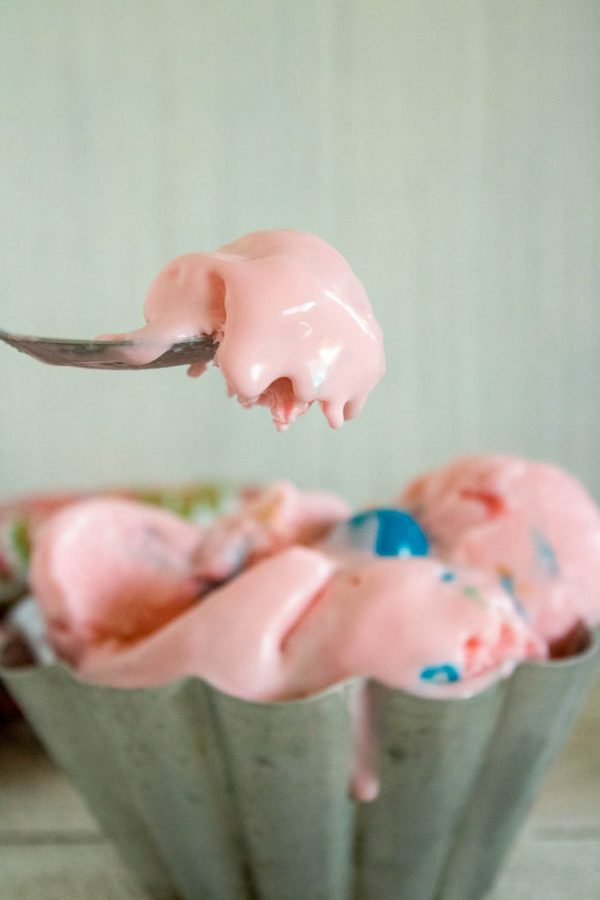 a metal spoon of pink bubblegum ice cream with a bowl of ice cream in the background.