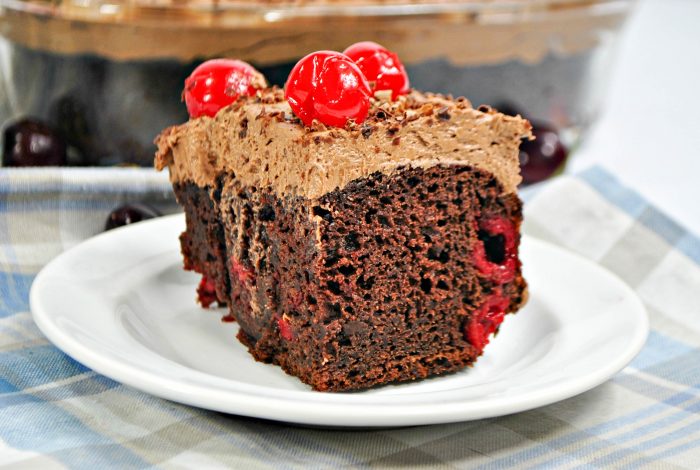 a slice of chocolate cherry cake with chocolate frosting on a white plate. 