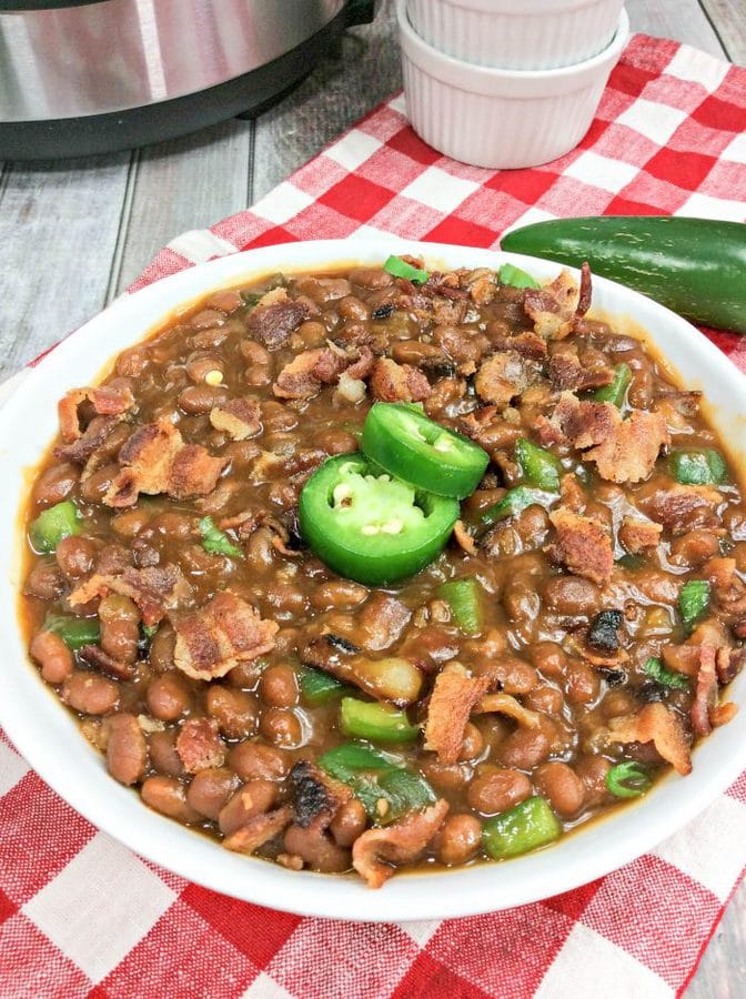 a large white bowl with baked beans topped with bacon and jalapenos. 