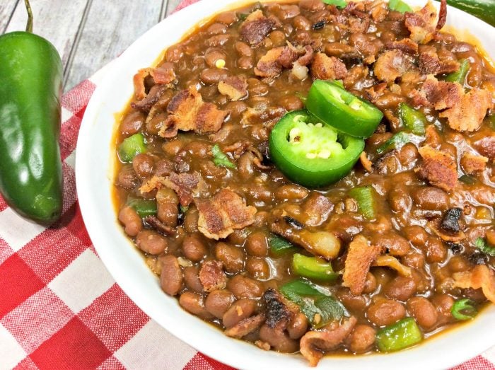 a close up of instant pot baked beans topped with bacon and jalapeno with a whole jalapeno in the background.