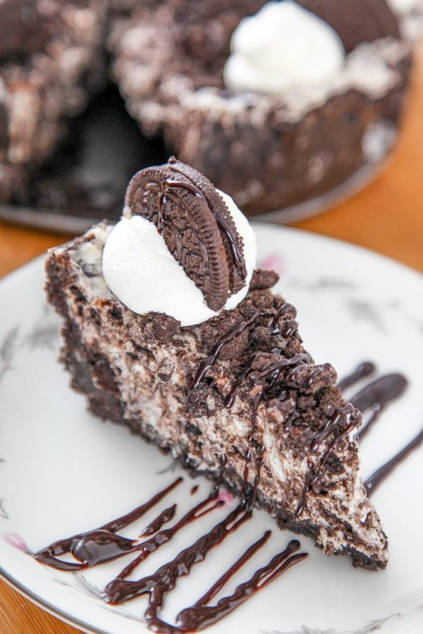 a slice of oreo cheesecake drizzled with hot fudge sauce, and garnished with an oreo cookie and whipped cream.