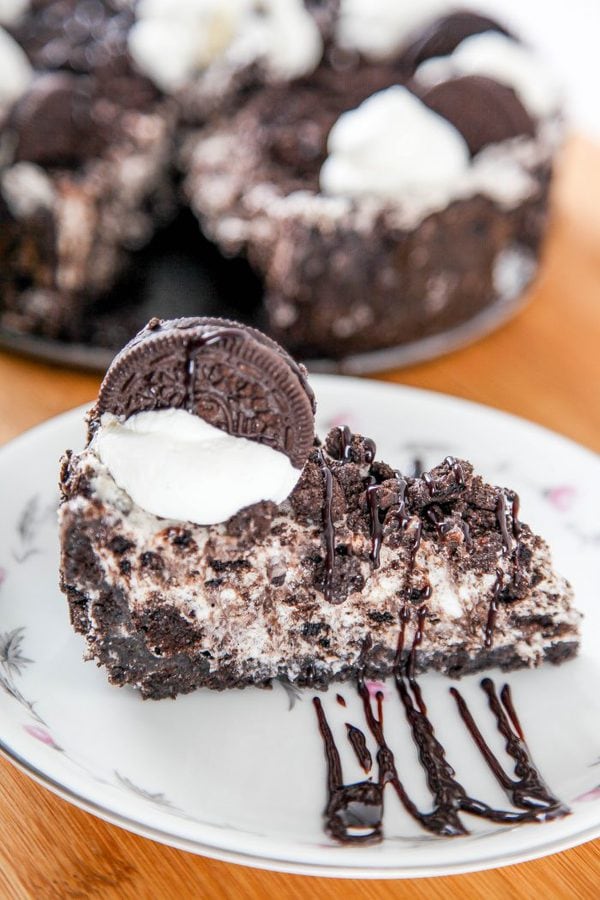 a sideways slice of oreo cheesecake topped with oreos, hot fudge, and whipped cream.