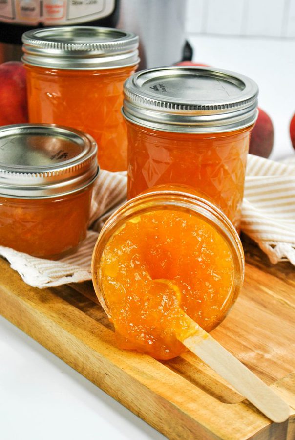 a glass jar of peach jam with more jars of jam in the background. 