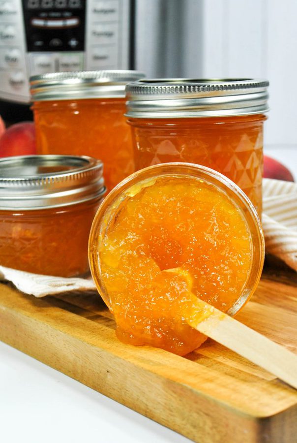 a popsicle stick scooping peach jam out of a glass mason jar. 