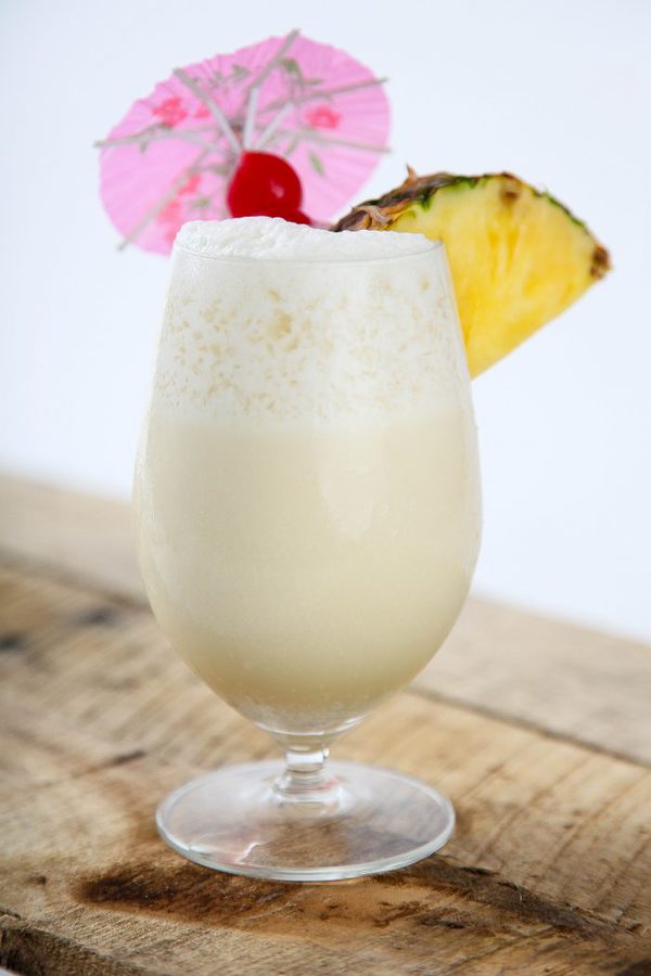 a large pina colada cocktail garnished with pineapple, cherries, and an umbrella on a wooden table.