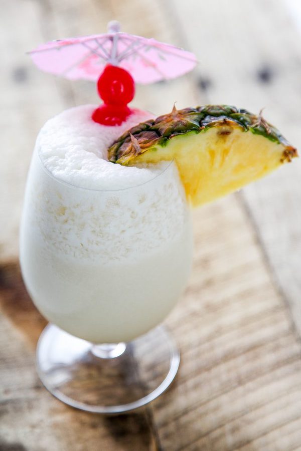 a frozen pina colada garnished with a slice of pineapple, maraschino cherries, and a pink cocktail umbrella.