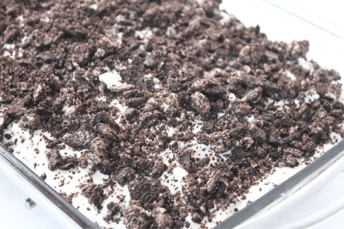 a chocolate cake topped with cool whip and crushed oreo cookies in a glass pan. 