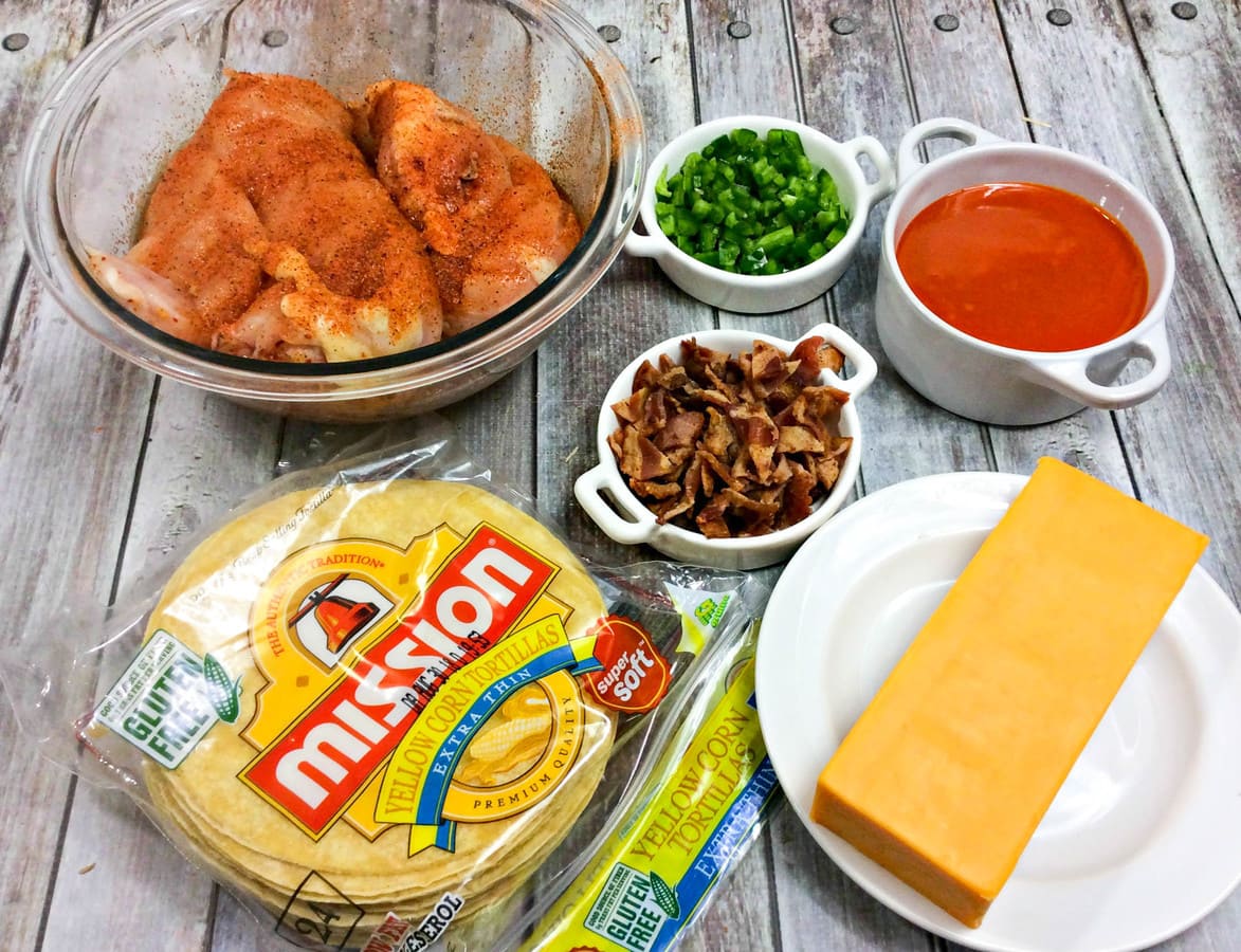 a picture showing corn tortillas, a block of cheddar cheese, Cajun chicken, buffalo sauce, and bacon. 