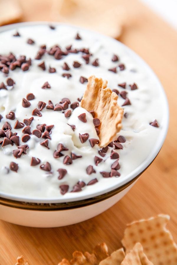 cannoli dip topped with chocolate chips and with a cannoli shell being dipped into it.