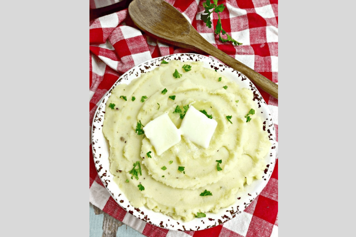 A bowl of mashed potatoes topped with two pats of  butter and parsley.