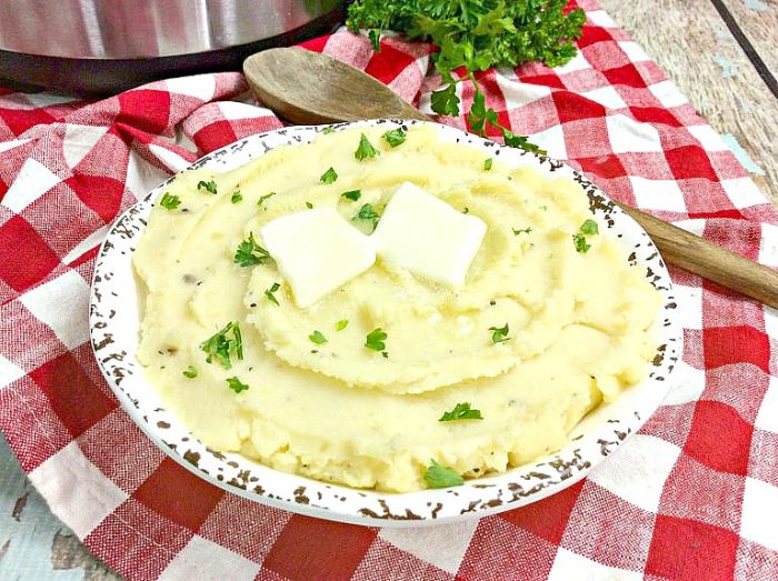 a white bowl of mashed potatoes topped with butter and parsley with an instant pot in the background.