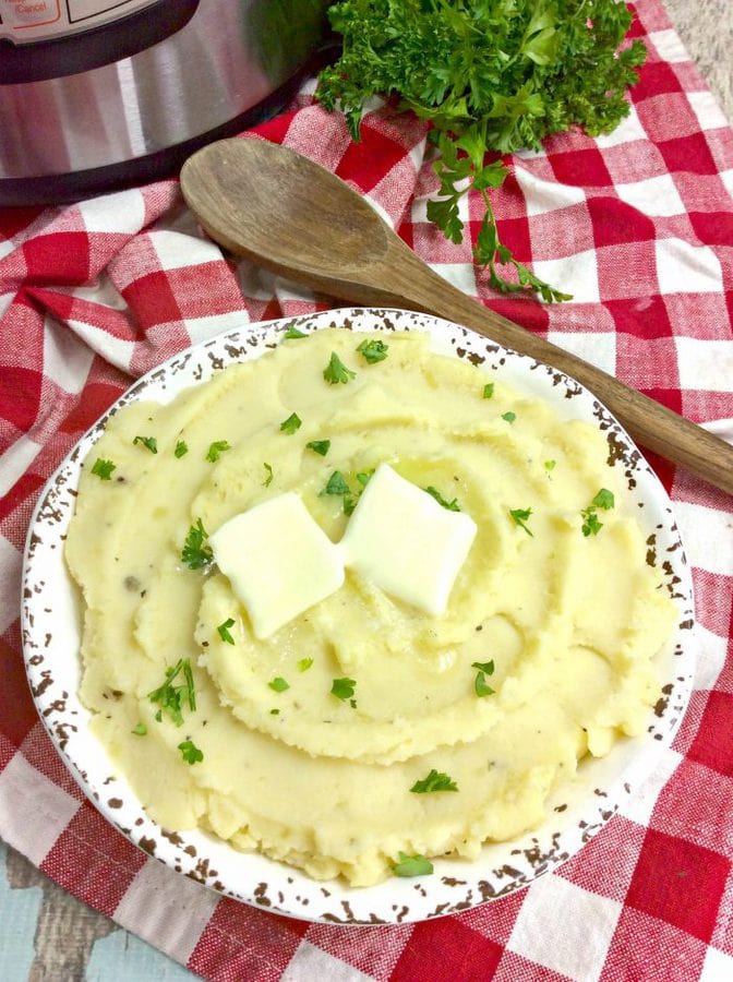 instant pot mashed potatoes topped with butter with a wooden spoon and parsley in the background.