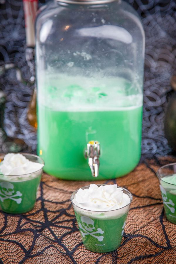 green polyjuice potion topped with whipped cream with a large drink dispenser in the background.