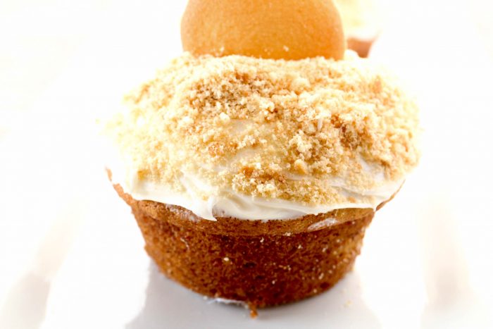 a closeup of a banana cupcake topped with vanilla icing and vanilla wafer cookie crumbs.