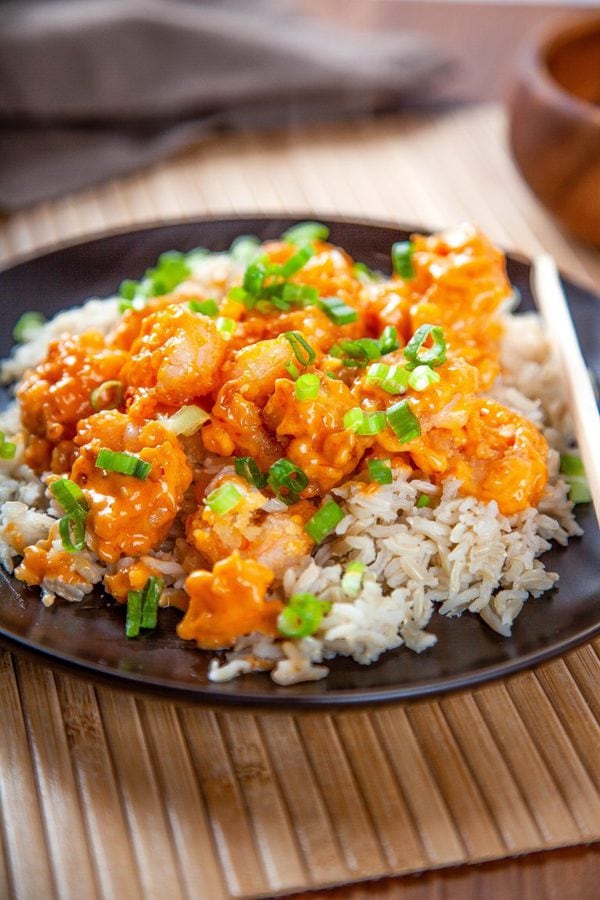A plate of rice topped with bang bang shrimp and garnished with green onions.