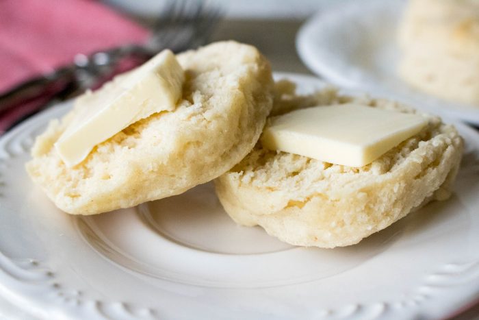 a closeup of buttermilk biscuits topped with butter on a white plate.