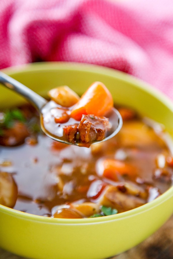 a closeup of beef stew with carrots on a metal spoon.