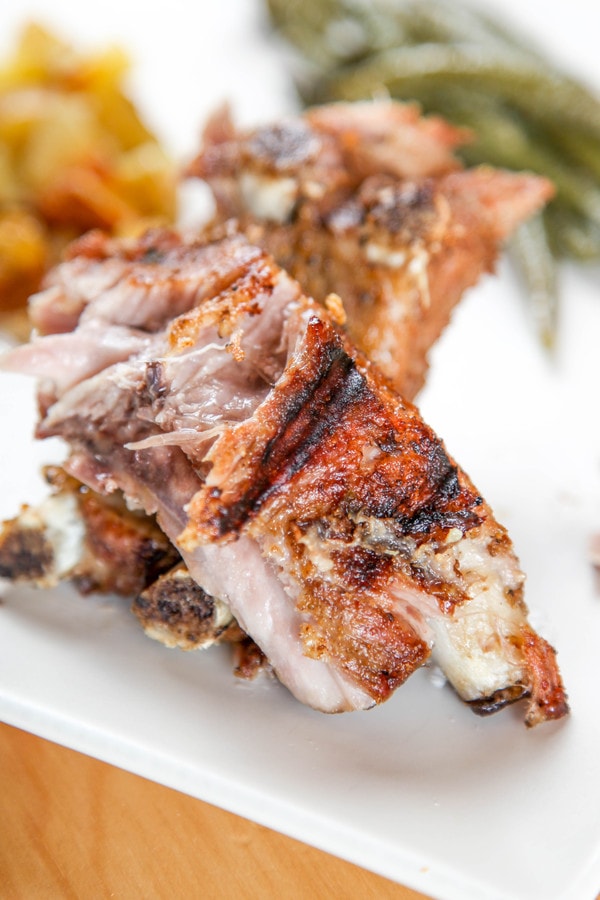 a charred rib with dry rub with potatoes and green beans in the background.