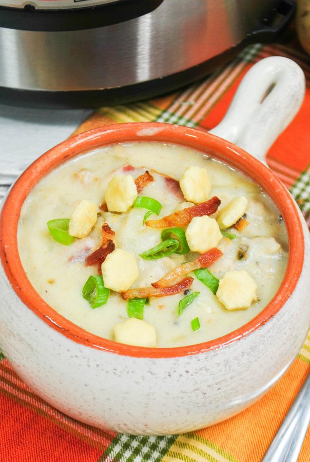 a bowl of new england clam chowder topped with bacon, green onions,and oyster crackers