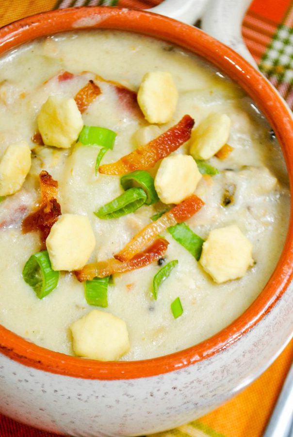 a close up of clam chowder in a bowl topped with strips of bacon, oystery crackers, and green onions.