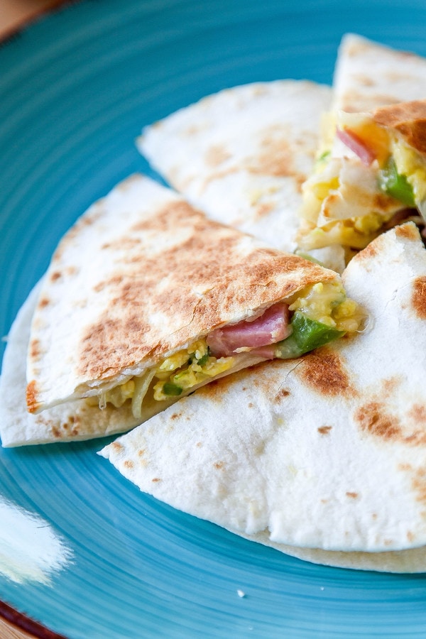a triangle of a breakfast quesadilla filled with eggs, cheese, ham, and green pepper. 