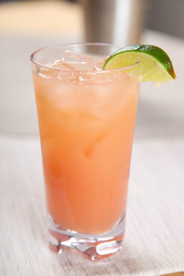 a side view of a grapefruit greyhound cocktail with ice and a lime wedge. 