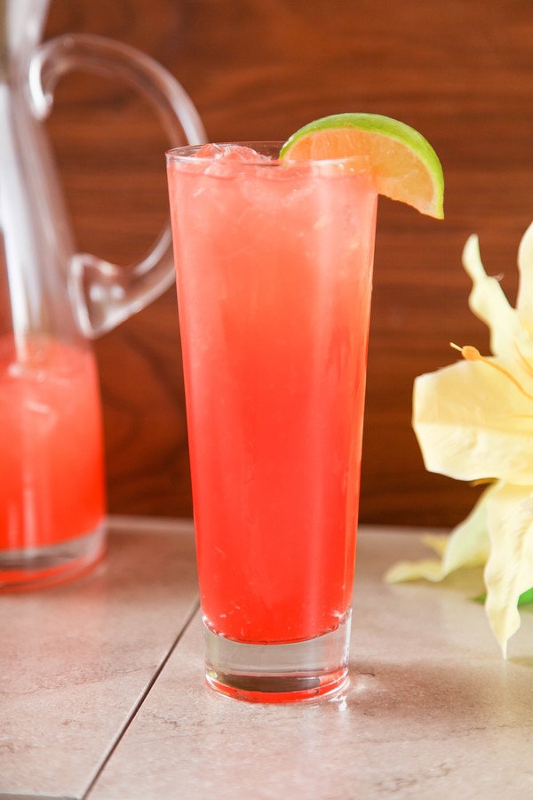 a tall sea drink garnished with a lime wedge with a pitcher in the background.