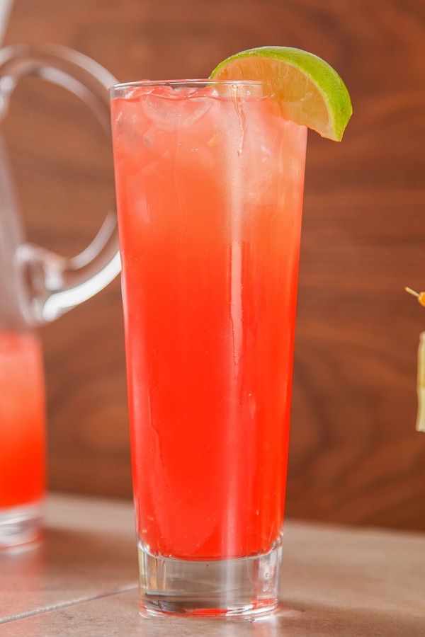 a sea breeze cocktail garnished with a lime wedge in a very tall glass.