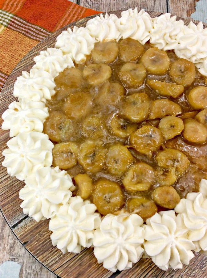 a cheesecake topped with caramelized bananas and piped homemade whipped cream on a wooden surface. 