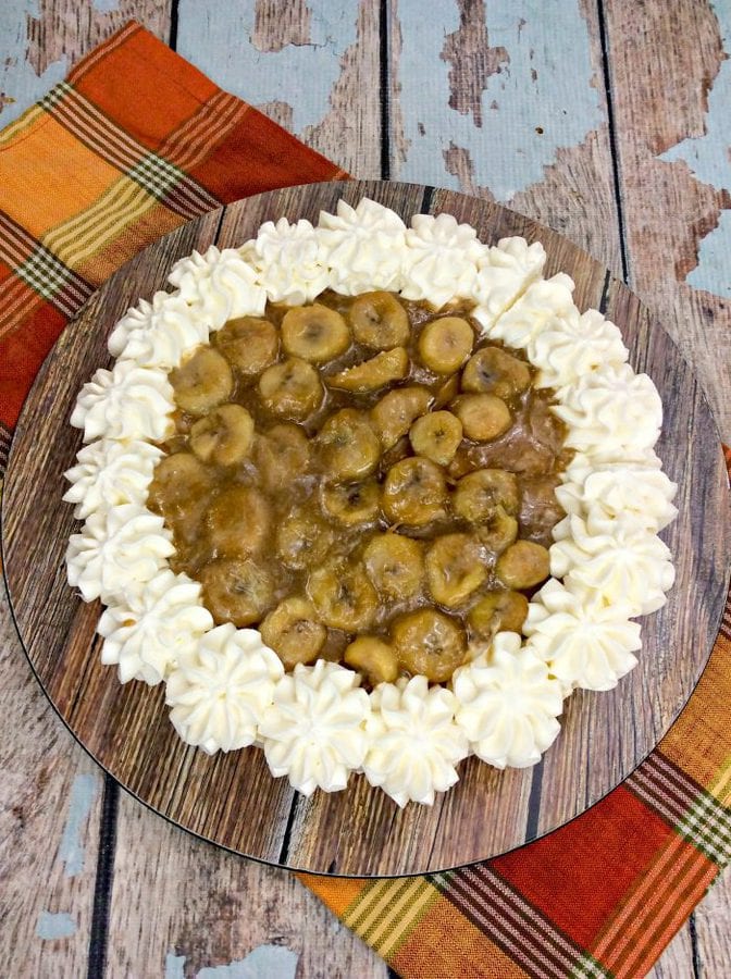 an overhead view of a cheesecake with caramelized bananas and piped whipped cream. 