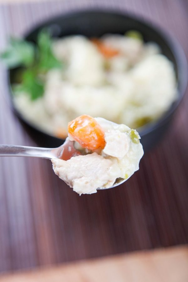 a spoon holding chicken and dumplings with carrots and celery with a bowl blurred in the background.